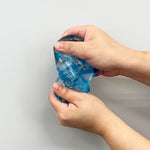 Hands squeezing a blue Chilly Cubeagainst a plain background