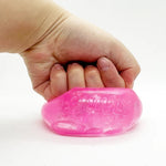 A hand squeezing a translucent pink squishy toy with embossed lettering Chilly Cube on a plain white background.
