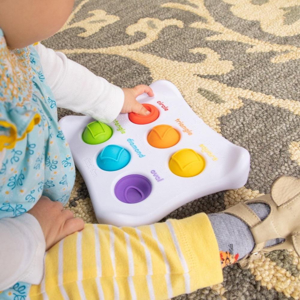 An infant sitting on the floor pressing a colourful silicone pop-it set in a plastic tray