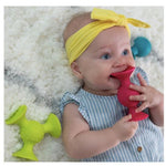 Baby lying on a white surface with colorful silicone teethers