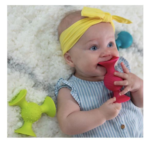 Baby lying on a white surface with colorful silicone teethers