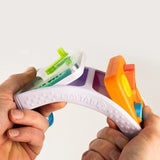 A close-up of a person's hands holding a PLAYTAB sensory toy, showing its white textured handle and colorful plastic inserts in green, blue, orange, and purple against a plain white background.