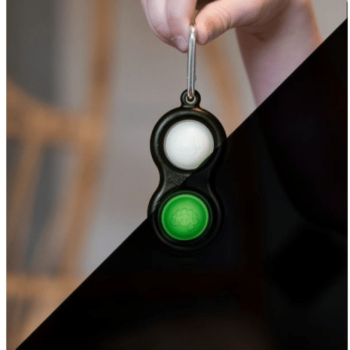 Black keychain with green and white buttons held by a hand against a blurred background