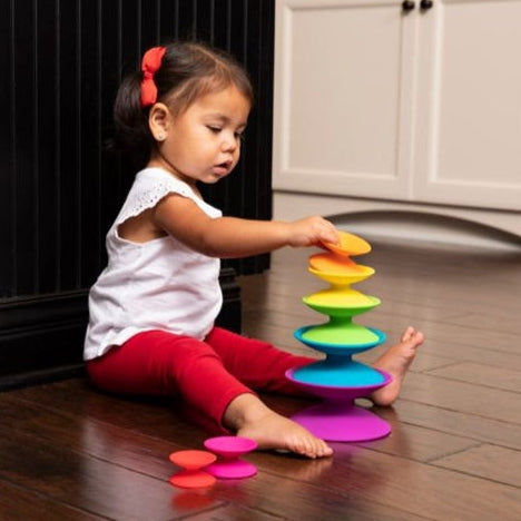 Child playing with a colorful stacking toy on a wooden floor.