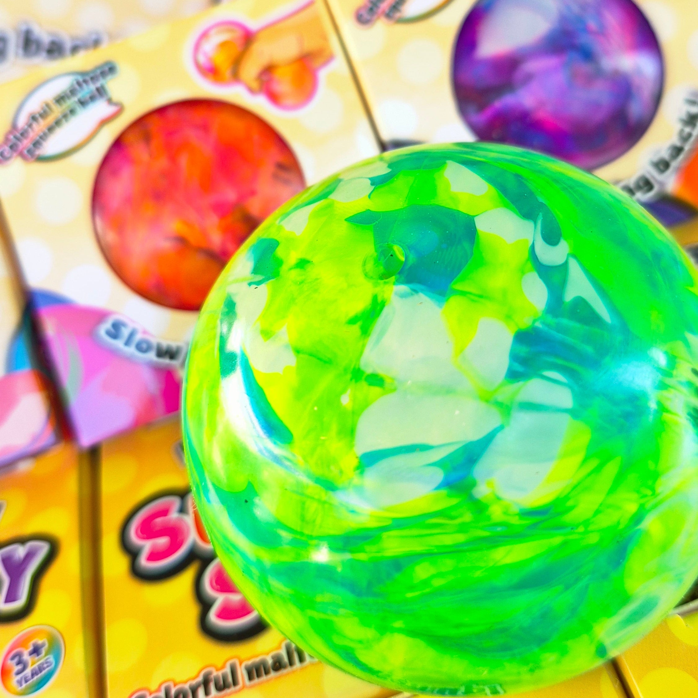 A close-up of a translucent, glossy green and blue marbled ball in the foreground, with multiple yellow candy boxes labeled 'SUGARY SOFT' 