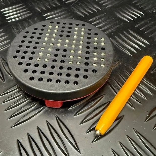 Black perforated tool with a yellow handle on a metallic surface