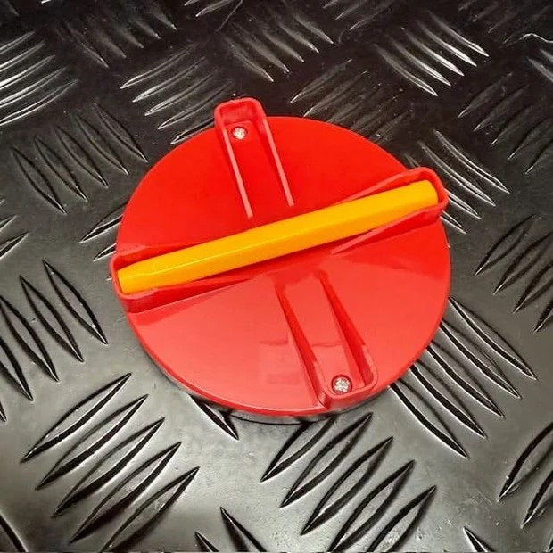 A red circular plastic pad with a yellow writing stylus across the center, photographed on a black diamond-plate metal surface.