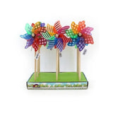 Colourful wooden pinwheel toys with striped and polka-dot patterns, displayed on a green base with a decorative border, set against a plain white background.