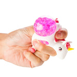 Hand holding a unicorn-themed squishy toy with a pink water beads popping out of it's sides on a white background