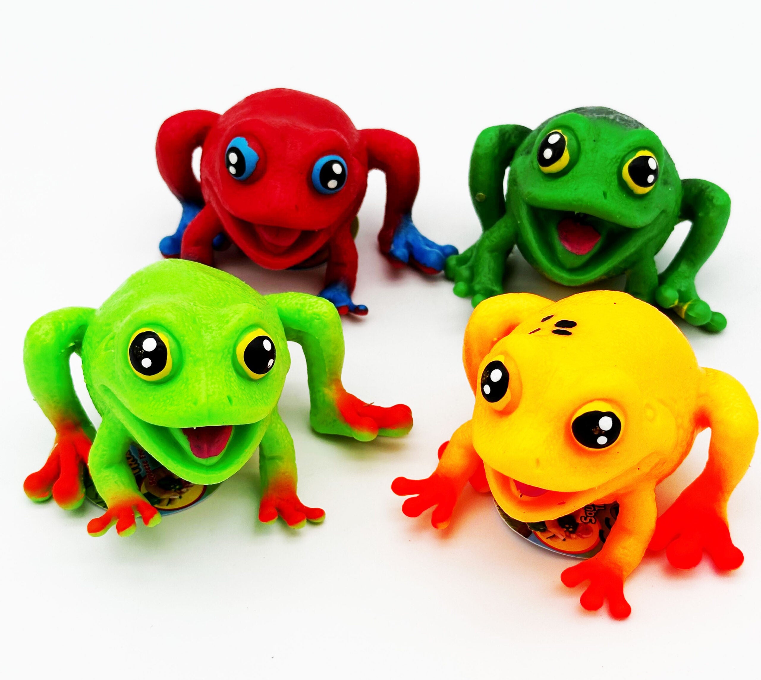 Four frog toys in red, green, yellow, and orange-red, arranged on a plain white background.